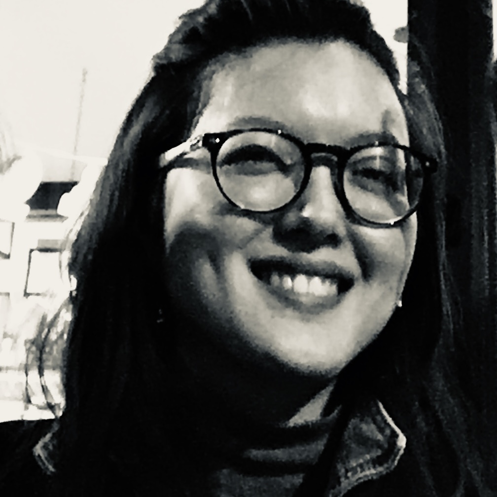 An Asian woman with shoulder-length hair and black round glasses, looking at the camera and smiling.